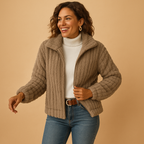 Femme souriante portant une veste en laine beige, col roulé blanc et jeans, posant sur fond beige. Mode automne-hiver, style décontracté.