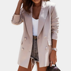 Femme portant un blazer beige élégant, t-shirt blanc, short en jean déchiré, montre-bracelet et sac à main. Mode chic et décontractée.