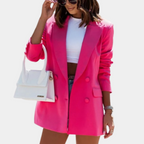 Femme portant un blazer rose vif, t-shirt blanc, short en jean, lunettes de soleil et sac à main blanc. Mode tendance, style chic et moderne.