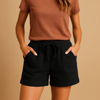 Femme portant un t-shirt marron et un short noir avec poches, sur fond beige. Mode décontractée, tenue estivale, style minimaliste.