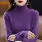 Femme portant un pull col roulé violet, boucles d'oreilles pendantes, assise sur un canapé en cuir. Mode automne-hiver, élégance féminine.