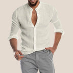 Homme portant une chemise en lin blanc à col mao, manches retroussées, avec un pantalon gris. Mode masculine élégante et décontractée.
