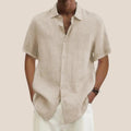Homme portant une chemise en lin beige à manches courtes, col ouvert, avec un pantalon blanc. Mode estivale élégante et décontractée.