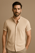 Homme portant une chemise beige à manches courtes, col mao, sur fond neutre. Mode masculine élégante, style décontracté chic.