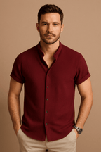 Homme portant une chemise bordeaux à manches courtes, posant devant un fond beige. Mode masculine élégante, style décontracté chic.