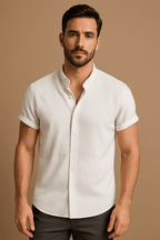 Homme portant une chemise blanche à manches courtes, col mao, sur fond beige. Mode masculine élégante, style décontracté chic.