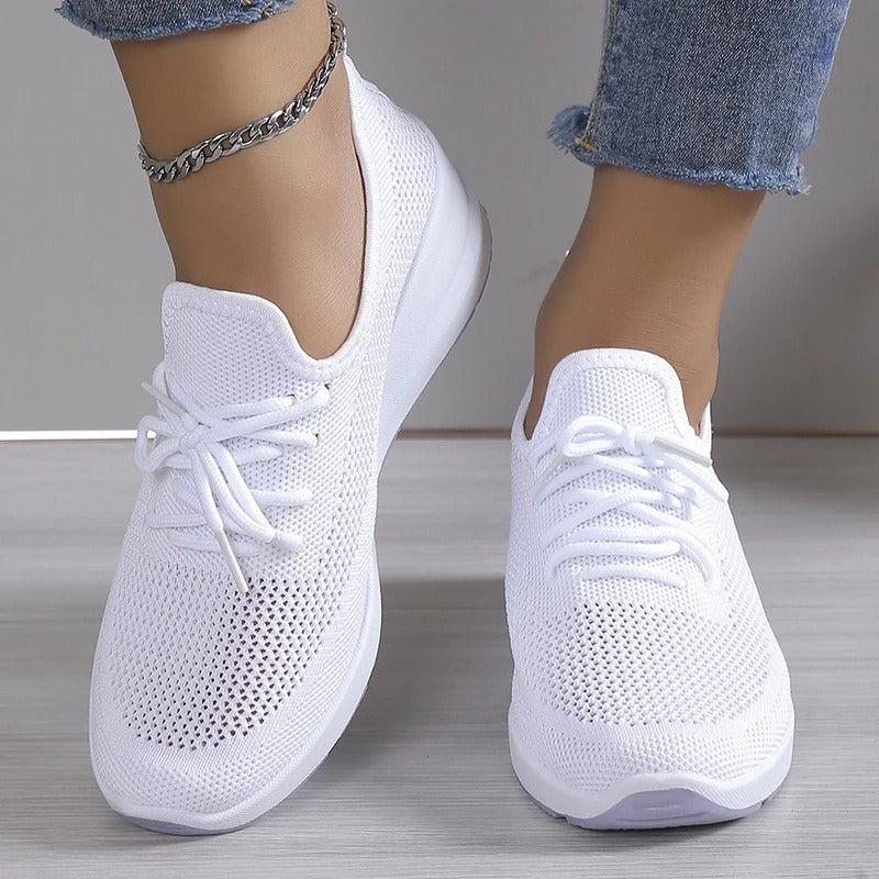 Chaussures de sport blanches en maille respirante, portées avec un jean décontracté. Sneakers légères et modernes pour un style urbain tendance.
