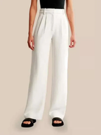 Pantalon large blanc pour femme, taille haute, avec pinces, porté avec un haut noir sans manches et des sandales noires. Mode élégante et moderne.