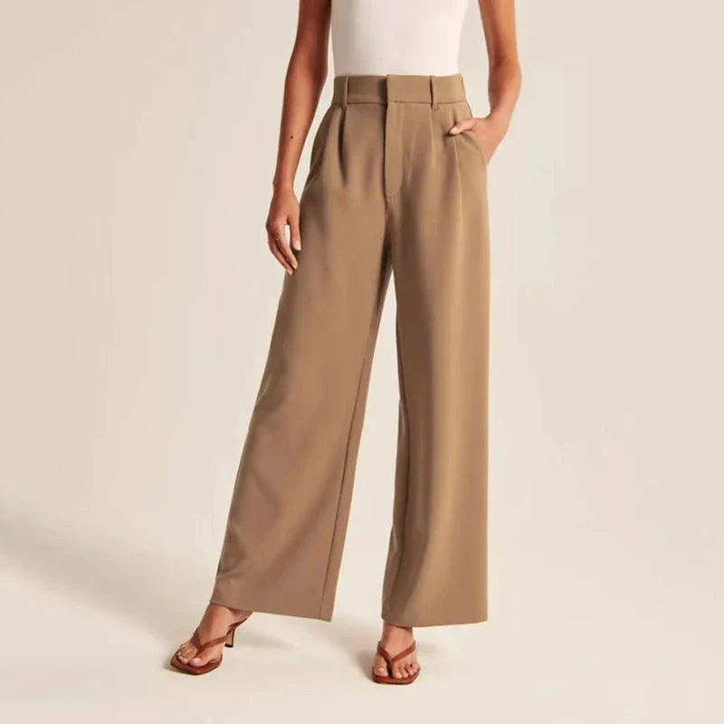 Pantalon large beige pour femme, taille haute, avec poches, porté avec un haut blanc sans manches et des sandales marron. Mode élégante et décontractée.