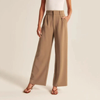 Pantalon large beige pour femme, taille haute, avec poches, porté avec un haut blanc sans manches et des sandales marron. Mode élégante et décontractée.