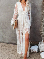 Robe longue en dentelle blanche avec manches longues et fente, portée par une femme blonde. Style bohème chic, idéal pour mariage ou plage.