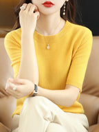 Femme portant un pull jaune en cachemire, assise sur un canapé beige, accessoirisée de bijoux élégants. Mode automne, style chic et décontracté.
