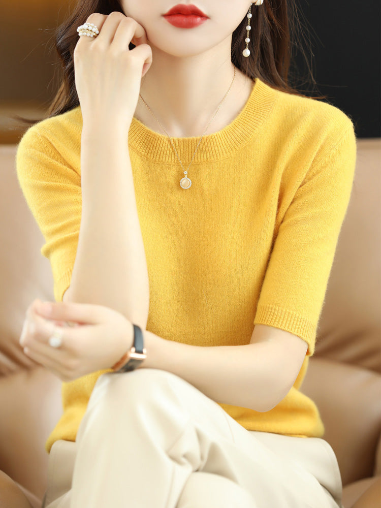 Femme portant un pull jaune en cachemire, assise sur un canapé beige, accessoirisée de bijoux élégants. Mode automne, style chic et décontracté.