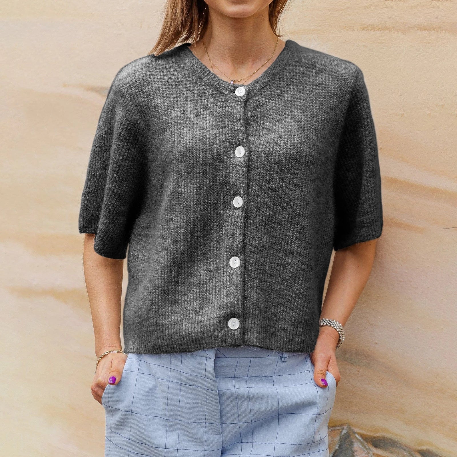 Femme portant un cardigan gris en tricot avec boutons blancs, associée à un pantalon à carreaux bleus. Mode automne, tenue décontractée élégante.