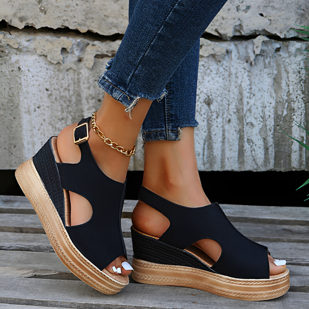 Sandales compensées noires élégantes avec semelle en corde, portées avec un jean déchiré et un bracelet doré. Mode estivale tendance et chic.