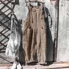 Salopette à carreaux marron suspendue sur un mur en métal, accompagnée d'un sac blanc et de chaussures blanches. Mode vintage, style décontracté.
