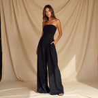 Femme en combinaison noire élégante, posant devant un fond beige drapé. Mode chic, tenue de soirée, style moderne.