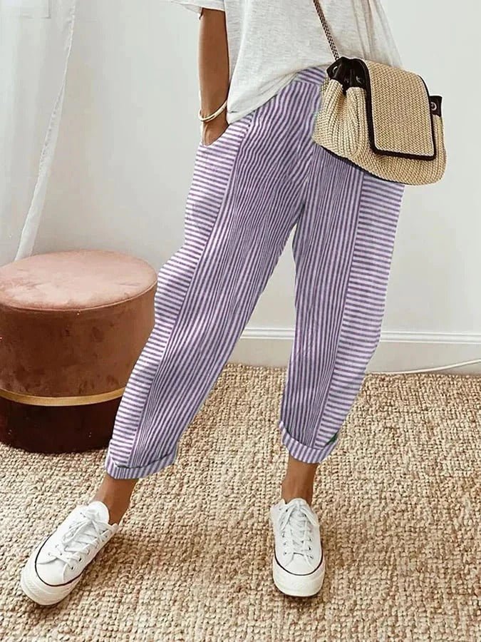 Pantalon rayé violet et blanc, style décontracté, avec un sac en osier et des baskets blanches sur tapis beige. Mode féminine tendance.