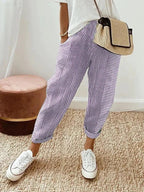 Pantalon rayé violet et blanc, style décontracté, avec un sac en osier et des baskets blanches sur tapis beige. Mode féminine tendance.