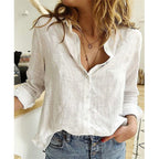 Femme portant une chemise blanche en lin, manches retroussées, avec un collier délicat, posant dans un intérieur moderne. Mode décontractée chic.