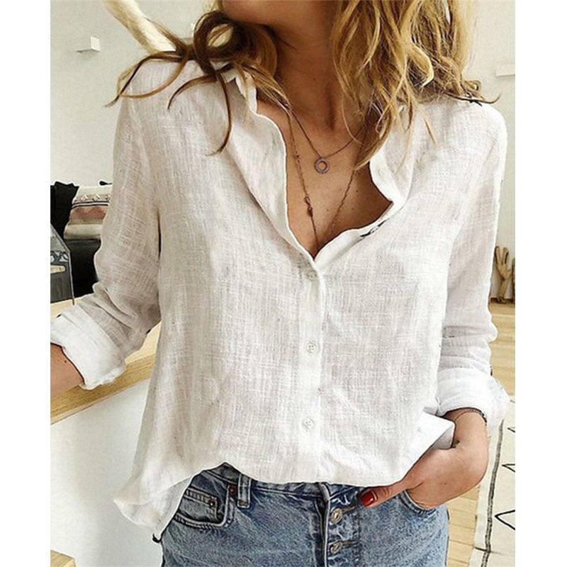 Femme portant une chemise blanche en lin, manches retroussées, avec un collier délicat, posant dans un intérieur moderne. Mode décontractée chic.