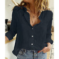 Femme portant une chemise noire en lin, manches retroussées, col ouvert, avec un collier délicat, posant dans un intérieur moderne et lumineux.