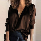 Femme portant un chemisier marron en satin avec un col en V profond, collier pendentif doré, tenue élégante et moderne, mode féminine chic.