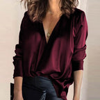 Femme portant un chemisier bordeaux en satin avec un col en V profond, manches longues, et un collier pendentif, tenue élégante et chic.