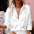 Femme en chemise blanche ample, assise sur un canapé rayé, portant des colliers dorés. Mode décontractée, style estival, cheveux blonds ondulés.