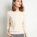 Femme portant un pull beige élégant, manches longues, col rond, posant contre un mur blanc. Mode féminine, style décontracté, tendance automne.