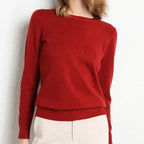 Pull rouge femme en laine, manches longues, col rond, porté avec un pantalon beige. Mode automne-hiver, style élégant et confortable.