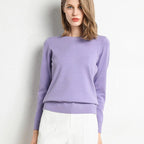 Femme portant un pull violet élégant, manches longues, col rond, assorti à un pantalon blanc. Mode féminine chic et moderne.