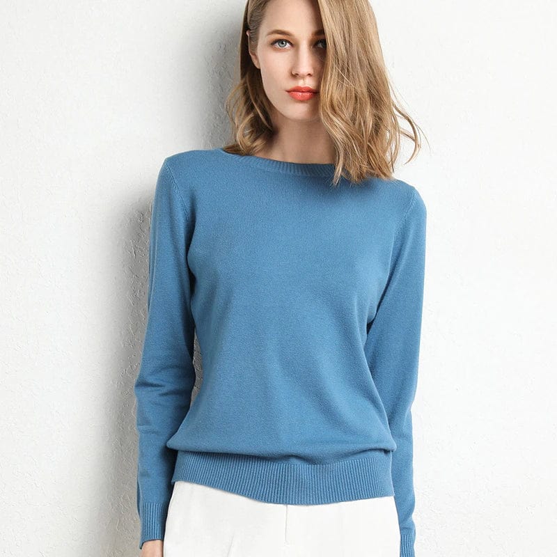 Femme portant un pull bleu élégant, manches longues, col rond, sur fond blanc. Mode féminine, tenue décontractée, style moderne.