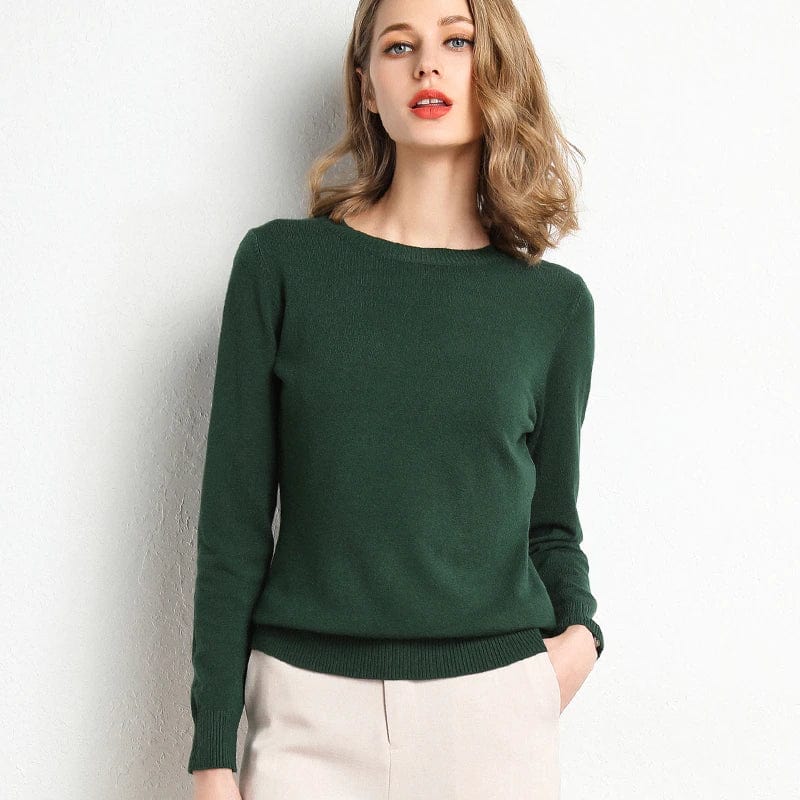 Jeune femme portant un pull vert élégant, manches longues, posant contre un mur blanc. Mode féminine, style automne-hiver, tenue décontractée.
