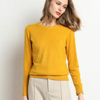 Jeune femme portant un pull jaune vif, manches longues, posant contre un mur blanc. Mode automne, style décontracté, élégance moderne.