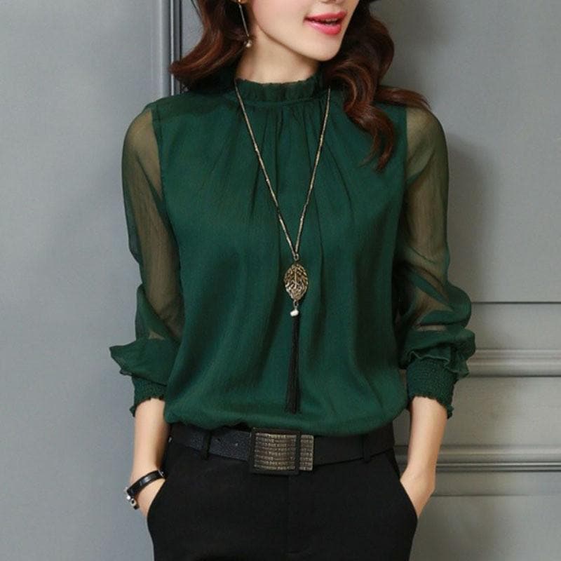 Femme portant un chemisier vert élégant avec manches transparentes, collier pendentif long, ceinture noire; mode chic et tendance.