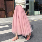Jupe longue en tulle rose portée avec un pull blanc et des mocassins roses à pompons, mode féminine élégante et tendance en ville.