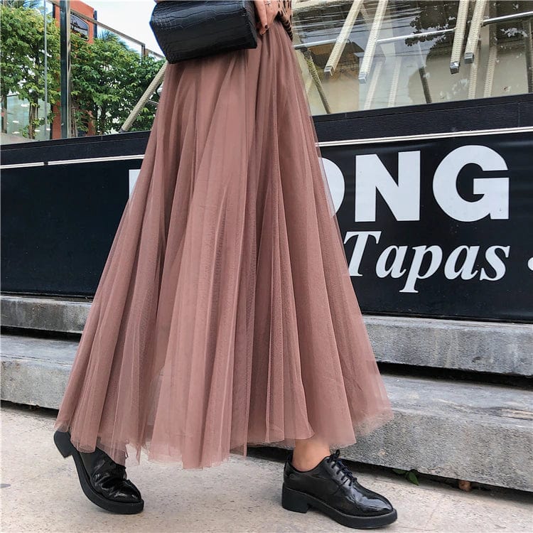 Jupe longue en tulle marron portée avec des chaussures noires élégantes, devant un restaurant moderne. Mode féminine chic et urbaine.