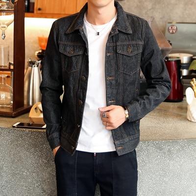 Homme portant une veste en jean noir, debout devant un comptoir moderne. Mode masculine, style décontracté, tendance vestimentaire.