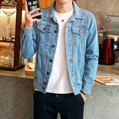 Homme portant une veste en jean bleu, tenant un smartphone dans un café moderne. Mode décontractée, style urbain, tendance vestimentaire.
