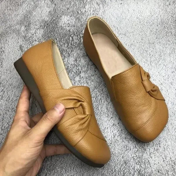Chaussures plates en cuir marron pour femmes avec nœud décoratif, semelle antidérapante, confortables et élégantes, posées sur fond gris.