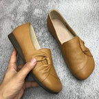 Chaussures plates en cuir marron pour femmes avec nœud décoratif, semelle antidérapante, confortables et élégantes, posées sur fond gris.