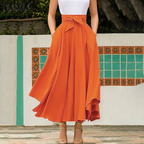 Femme en jupe longue orange élégante, ceinture nouée, posant devant un mur décoratif. Mode féminine, style chic, tenue estivale.