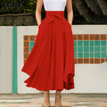 Robe longue rouge élégante avec ceinture nouée, portée par une femme debout devant un mur décoratif. Mode féminine, style chic, tendance été.