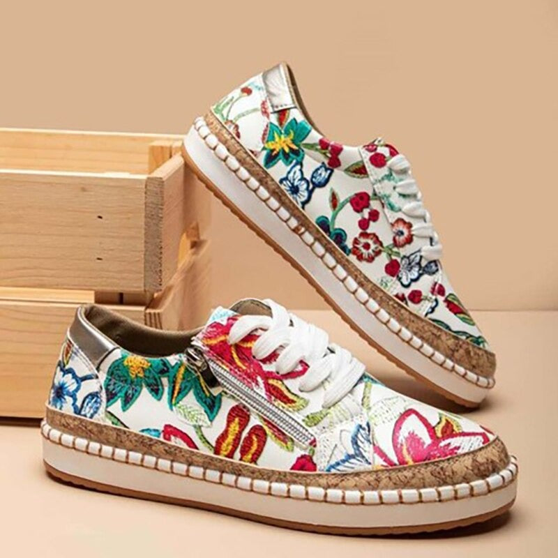Chaussures de sport blanches à motifs floraux colorés, semelles en liège, lacets blancs, posées devant une boîte en bois. Mode, tendance, confort.