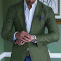 Homme en costume vert ajusté, chemise blanche, ajustant sa montre-bracelet argentée. Élégance masculine, mode formelle, style moderne.