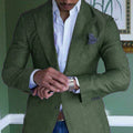 Homme élégant en costume vert ajustant sa montre-bracelet, chemise blanche, pochette grise, style chic, mode masculine, tenue formelle.