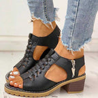 Sandales noires en cuir à talons blocs, avec lacets et fermeture éclair, portées avec un jean déchiré. Mode estivale élégante et confortable.