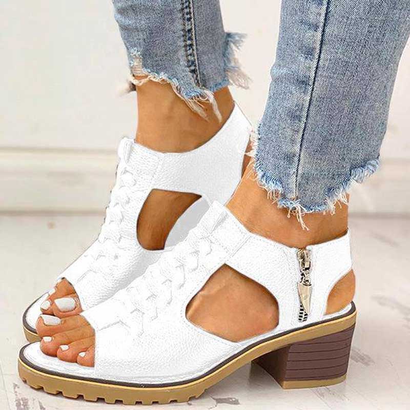 Chaussures blanches à talons blocs, ouvertes, avec fermeture éclair latérale, portées avec un jean effiloché. Mode féminine, tendance été.