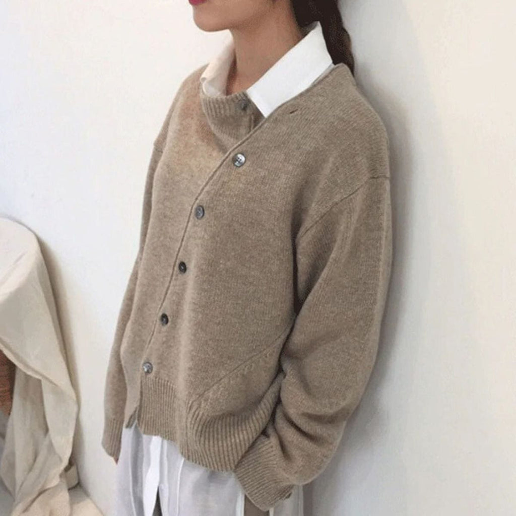 Femme portant un pull cardigan beige en laine avec boutons, sur une chemise blanche. Mode automne-hiver, tenue décontractée élégante.